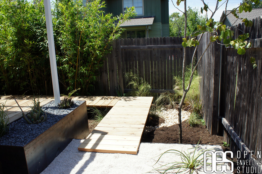 Design ideas for a mid-sized modern backyard partial sun xeriscape in Austin with gravel and a retaining wall.