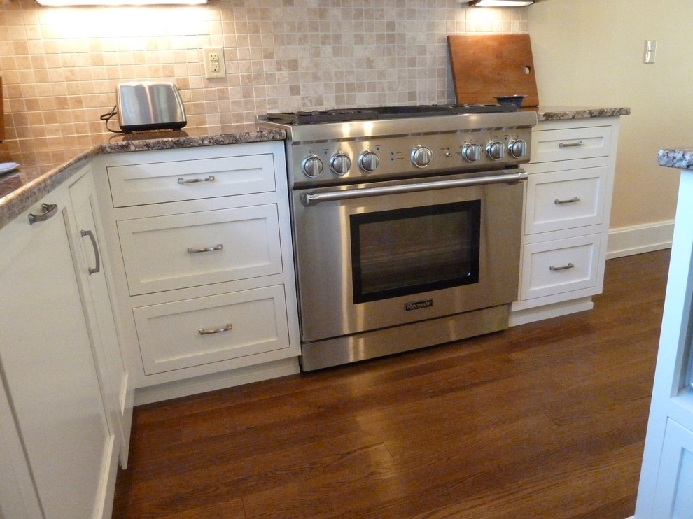 Inspiration for a mid-sized transitional l-shaped medium tone wood floor eat-in kitchen remodel in Indianapolis with an undermount sink, shaker cabinets, white cabinets, granite countertops, beige backsplash, stone tile backsplash, stainless steel appliances and an island