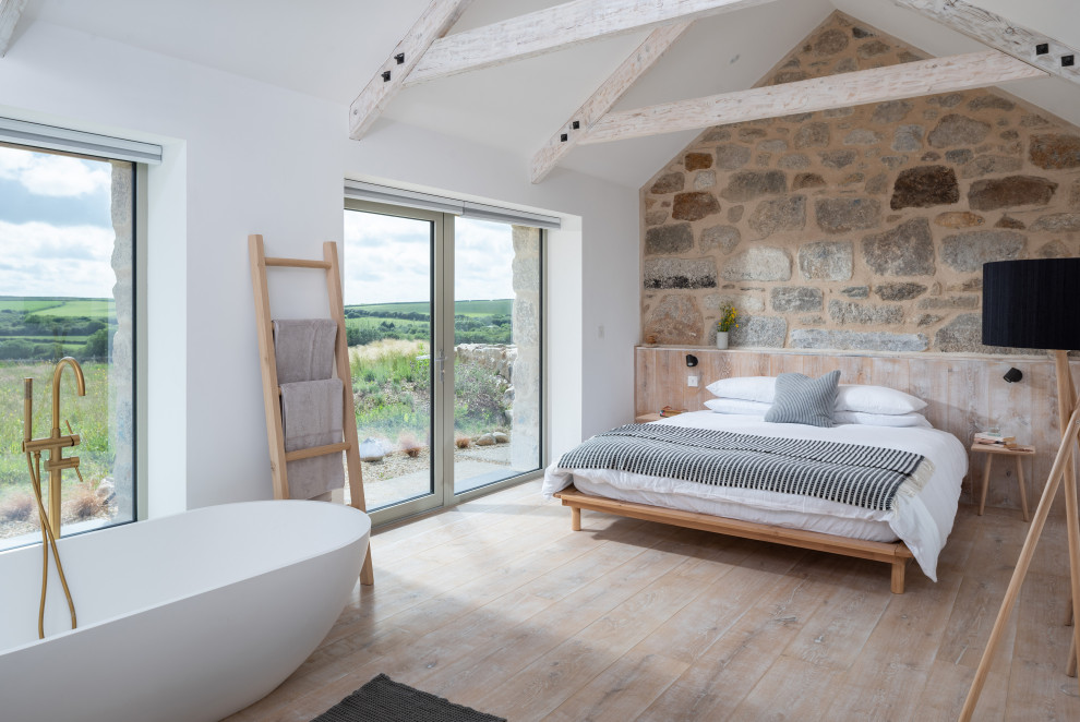 Photo of a large farmhouse master bedroom in Cornwall with white walls and light hardwood flooring.
