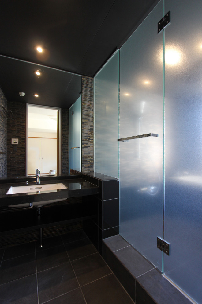 Inspiration for a mid-sized modern master bathroom in Other with open cabinets, black cabinets, a drop-in tub, an open shower, brown tile, mosaic tile, brown walls, porcelain floors, solid surface benchtops, black floor, a hinged shower door, black benchtops, a single vanity, a built-in vanity and timber.