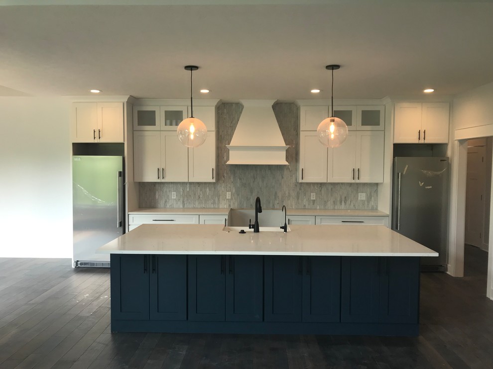 Inspiration for a large transitional single-wall dark wood floor and brown floor open concept kitchen remodel with a farmhouse sink, shaker cabinets, white cabinets, solid surface countertops, white backsplash, marble backsplash, stainless steel appliances, an island and white countertops