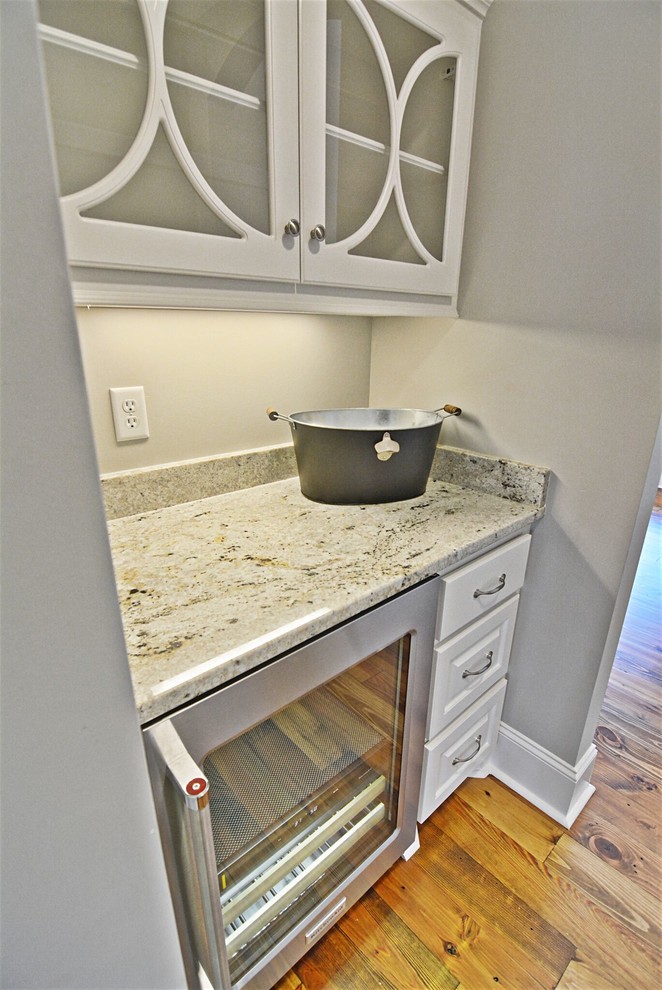 This is an example of a small transitional single-wall wet bar in Jackson with no sink, raised-panel cabinets, white cabinets, granite benchtops, light hardwood floors and brown floor.