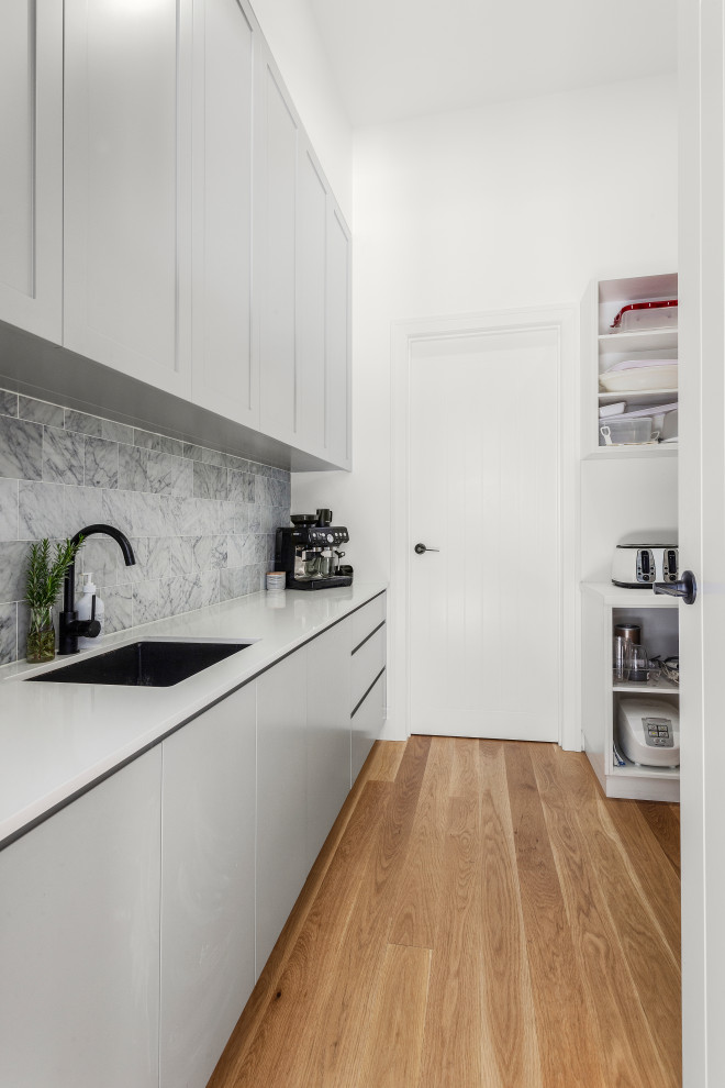 Large contemporary u-shaped open plan kitchen in Melbourne with a double-bowl sink, shaker cabinets, marble benchtops, grey splashback, marble splashback, black appliances, light hardwood floors, with island and grey benchtop.