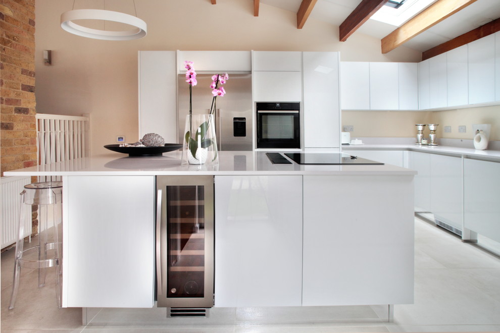 Large contemporary u-shaped open plan kitchen in Oxfordshire with a drop-in sink, flat-panel cabinets, white cabinets, quartzite benchtops, black appliances, porcelain floors and with island.