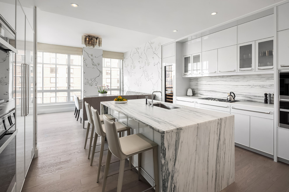 Inspiration for a mid-sized contemporary single-wall medium tone wood floor and brown floor open concept kitchen remodel in New York with an undermount sink, flat-panel cabinets, white cabinets, stone slab backsplash, an island, granite countertops, gray backsplash, stainless steel appliances and gray countertops