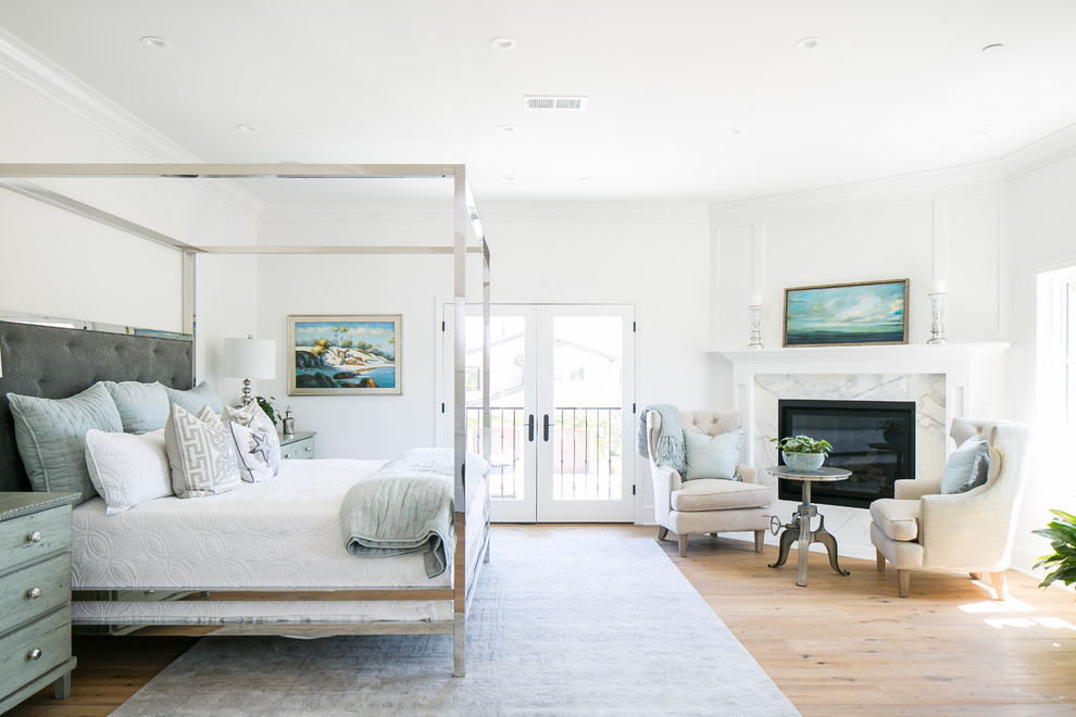 Design ideas for a beach style master bedroom in Orange County with white walls, light hardwood floors, a standard fireplace, a stone fireplace surround and beige floor.