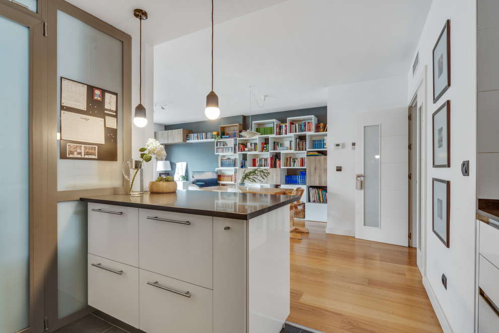 Mid-sized scandinavian galley eat-in kitchen in Madrid with a single-bowl sink, flat-panel cabinets, white cabinets, granite benchtops, grey splashback, metal splashback, stainless steel appliances, porcelain floors, with island, grey floor and grey benchtop.