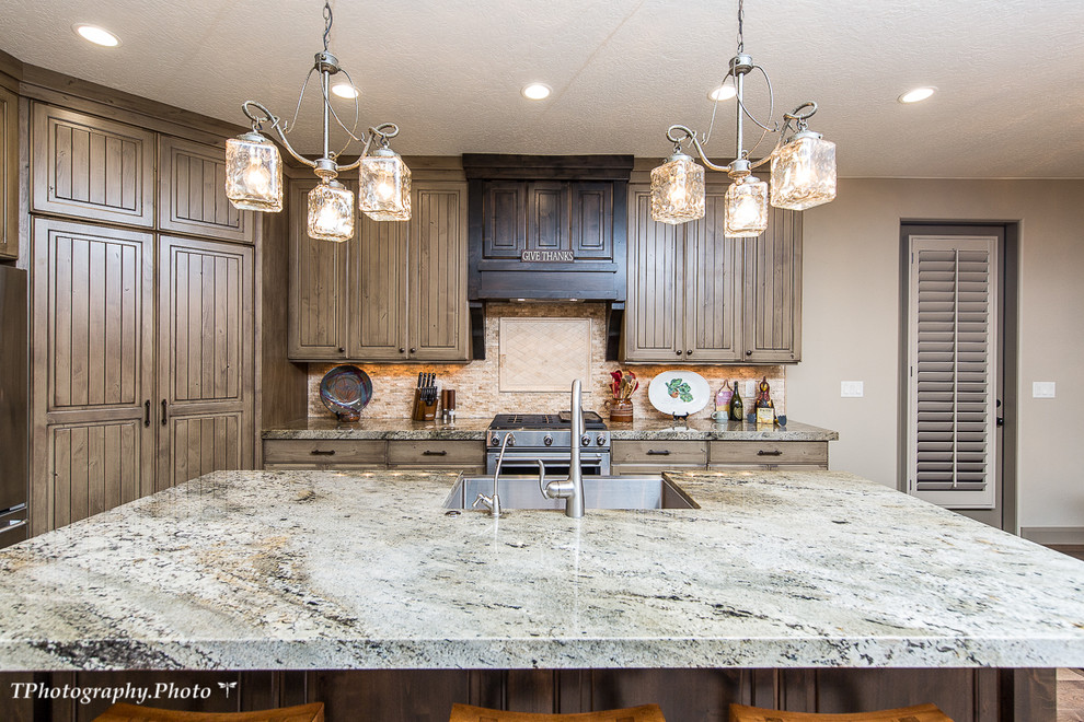 Photo of a large country l-shaped eat-in kitchen in Salt Lake City with a farmhouse sink, beaded inset cabinets, distressed cabinets, beige splashback, stainless steel appliances, with island, granite benchtops, travertine splashback, medium hardwood floors and brown floor.