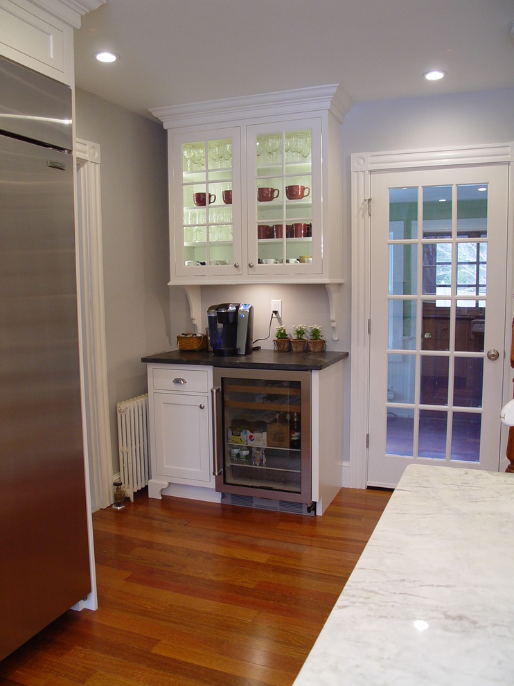 Example of a transitional enclosed kitchen design in Boston with a farmhouse sink, recessed-panel cabinets, white cabinets, granite countertops, white backsplash, subway tile backsplash, stainless steel appliances and an island