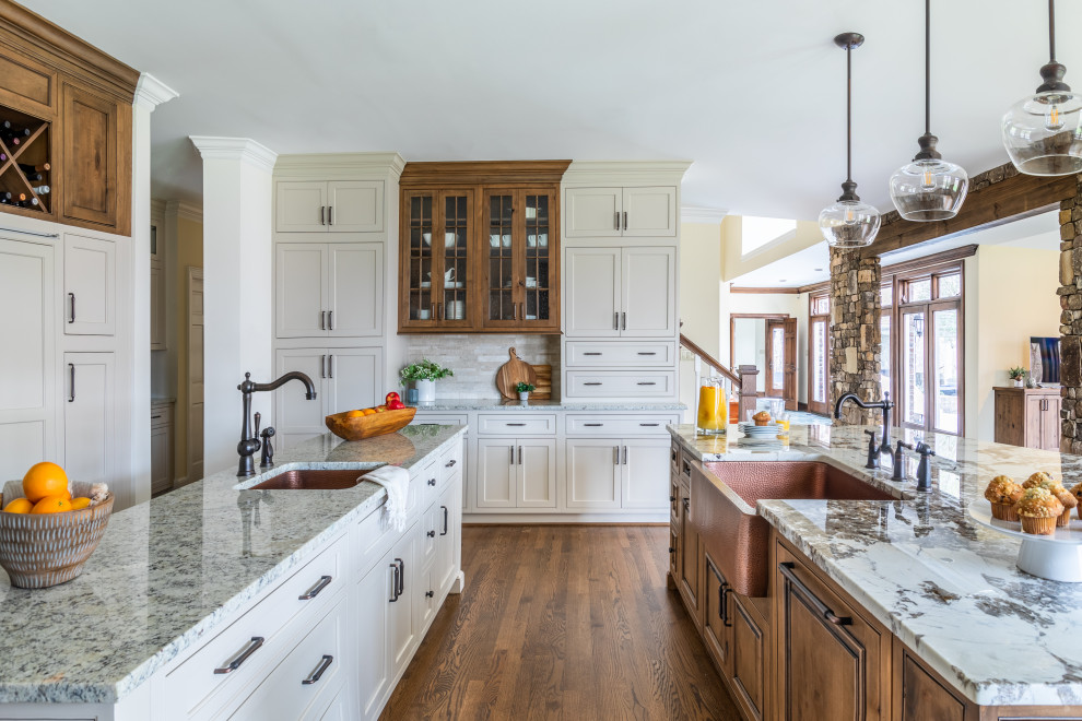 Example of a classic u-shaped dark wood floor and brown floor kitchen design with a farmhouse sink, shaker cabinets, white cabinets, two islands and gray countertops