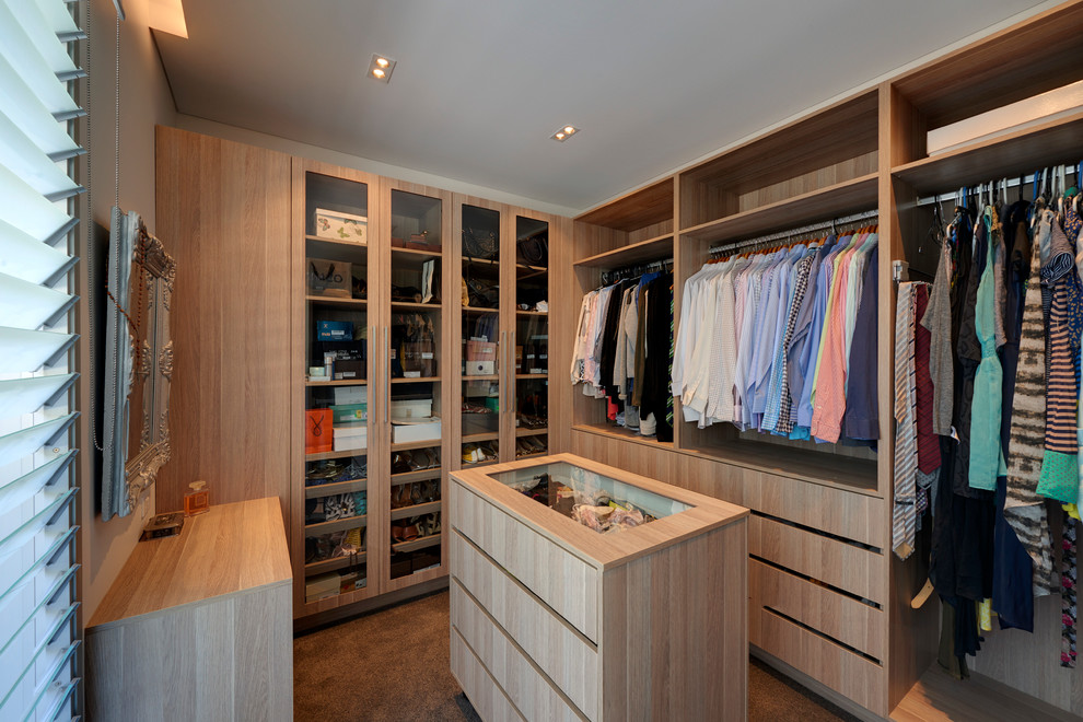 Photo of a large contemporary gender-neutral walk-in wardrobe in Sydney with glass-front cabinets, light wood cabinets and carpet.