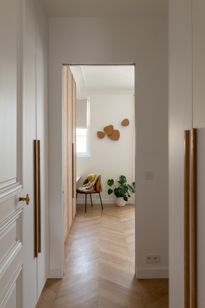 Cette image montre une grande chambre parentale blanche et bois design avec un mur blanc, parquet clair et dressing.