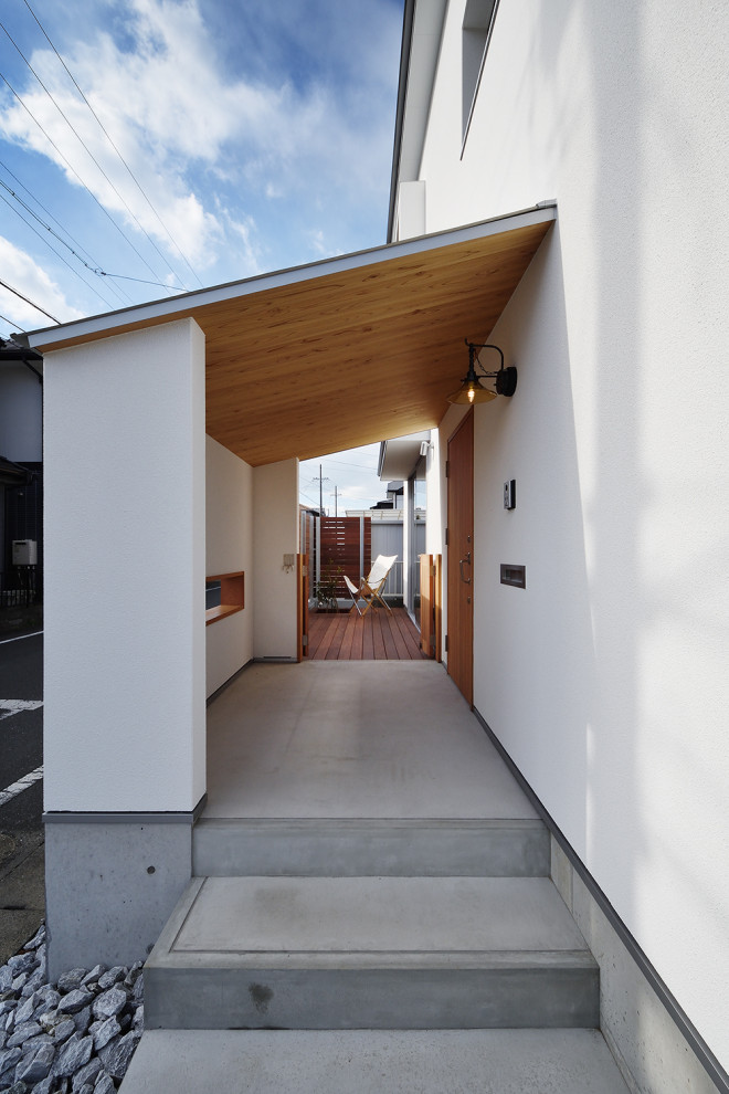На фото: входная дверь среднего размера в скандинавском стиле с белыми стенами, бетонным полом, одностворчатой входной дверью, входной дверью из дерева среднего тона, серым полом и деревянным потолком с