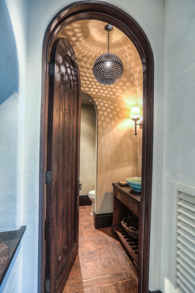 This is an example of a small mediterranean powder room in Houston with flat-panel cabinets, dark wood cabinets, a two-piece toilet, beige walls, terra-cotta floors, a vessel sink, wood benchtops and red floor.