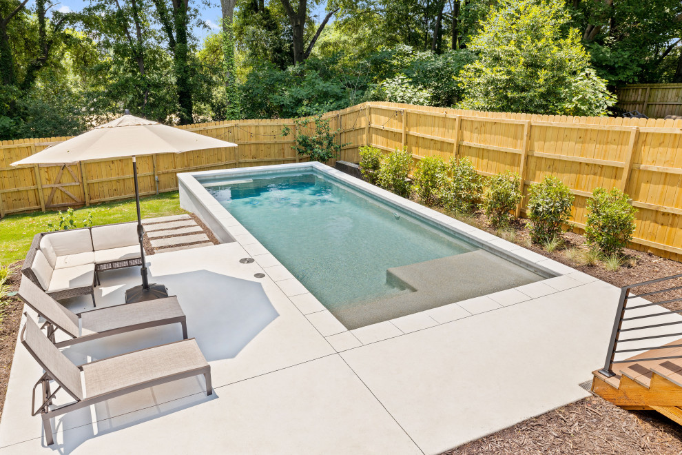 Bild på en mellanstor funkis rektangulär pool insynsskydd och på baksidan av huset, med stämplad betong