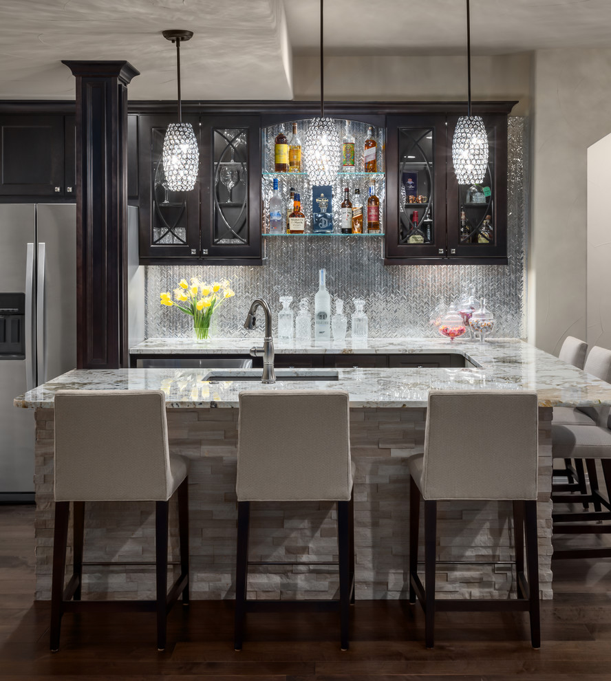 Photo of a mid-sized transitional u-shaped seated home bar in Denver with dark hardwood floors, brown floor, an undermount sink, glass-front cabinets, dark wood cabinets, granite benchtops, grey splashback, metal splashback and grey benchtop.