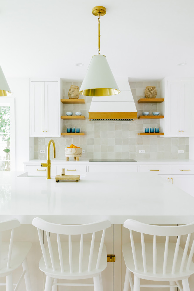 Large beach style l-shaped kitchen/diner in Other with a belfast sink, shaker cabinets, white cabinets, engineered stone countertops, beige splashback, mosaic tiled splashback, integrated appliances, light hardwood flooring, an island, brown floors and white worktops.
