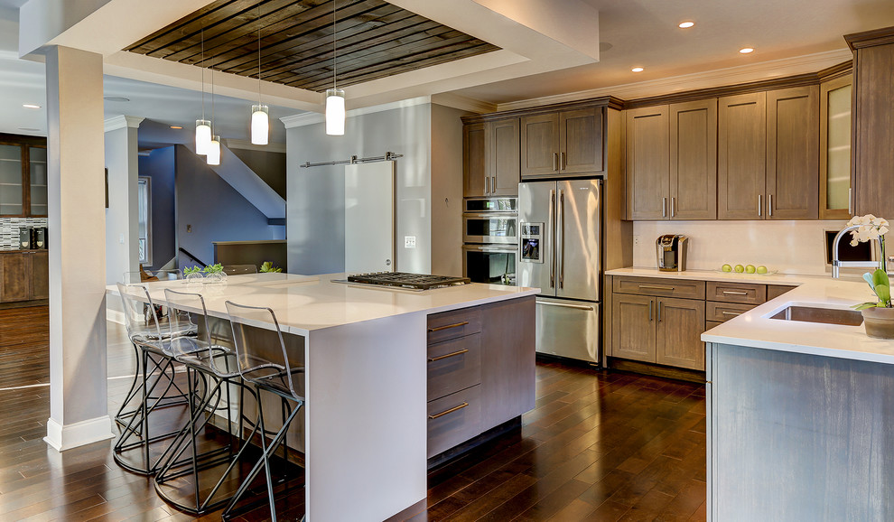 Example of a transitional dark wood floor kitchen design with an undermount sink, gray cabinets, quartzite countertops, white backsplash, porcelain backsplash, stainless steel appliances and an island