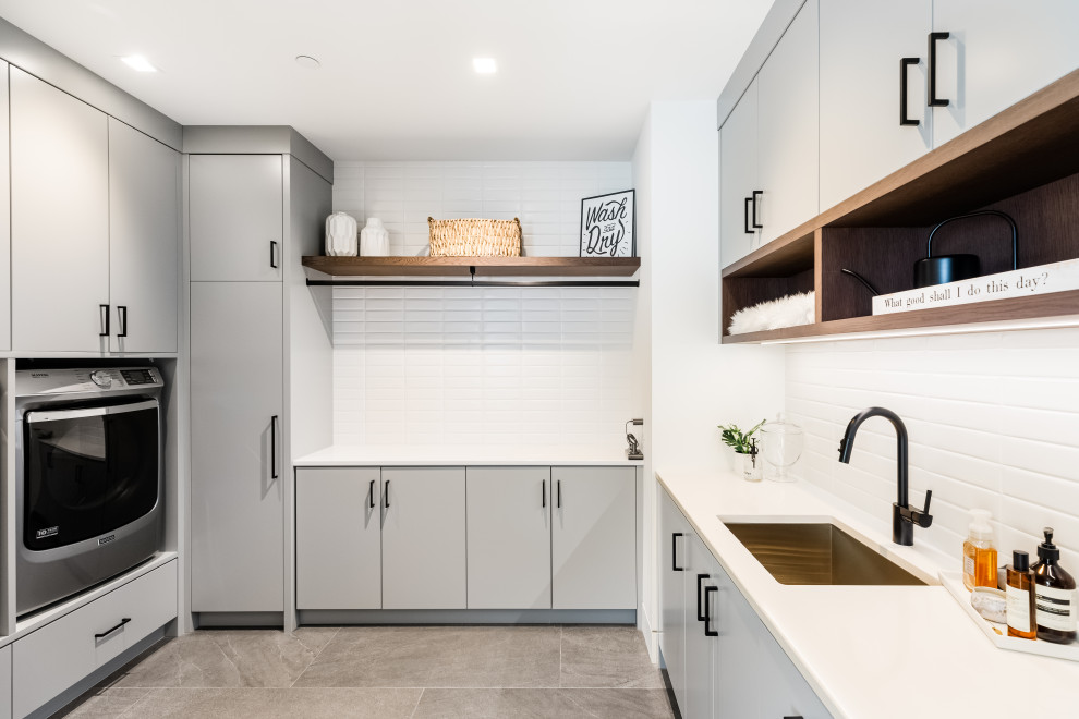 Design ideas for a large contemporary u-shaped separated utility room in Vancouver with a submerged sink, flat-panel cabinets, grey cabinets, engineered stone countertops, white splashback, metro tiled splashback, white walls, porcelain flooring, a side by side washer and dryer, grey floors and white worktops.