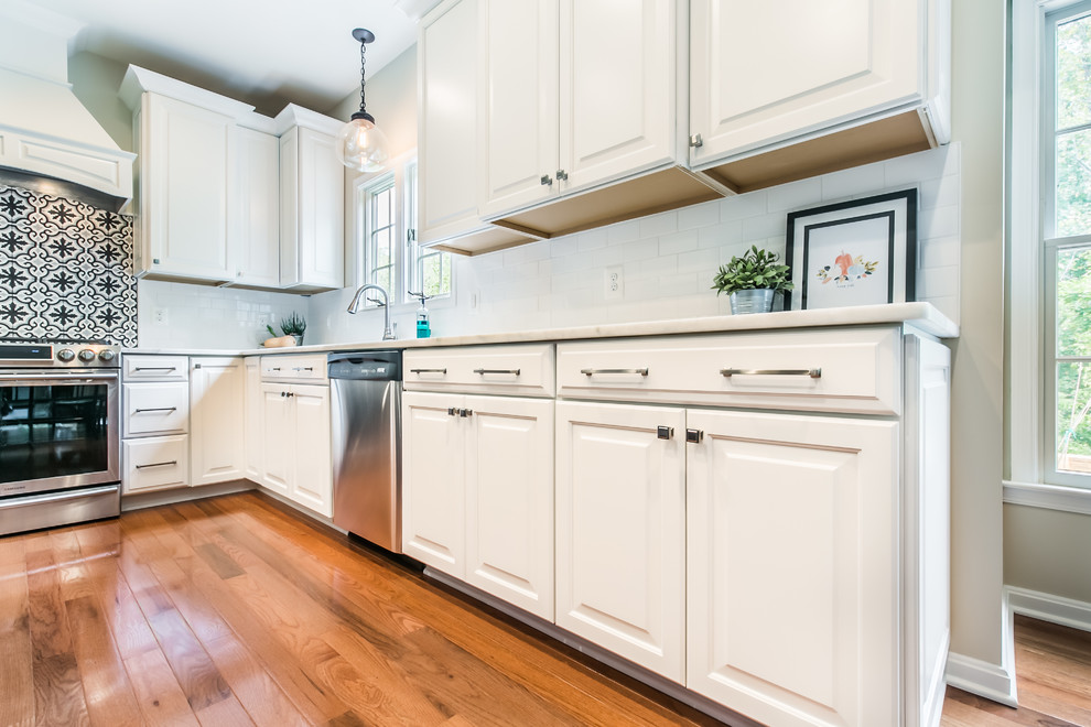 Large transitional l-shaped eat-in kitchen in DC Metro with an undermount sink, raised-panel cabinets, white cabinets, quartz benchtops, white splashback, cement tile splashback, stainless steel appliances, medium hardwood floors, with island and brown floor.