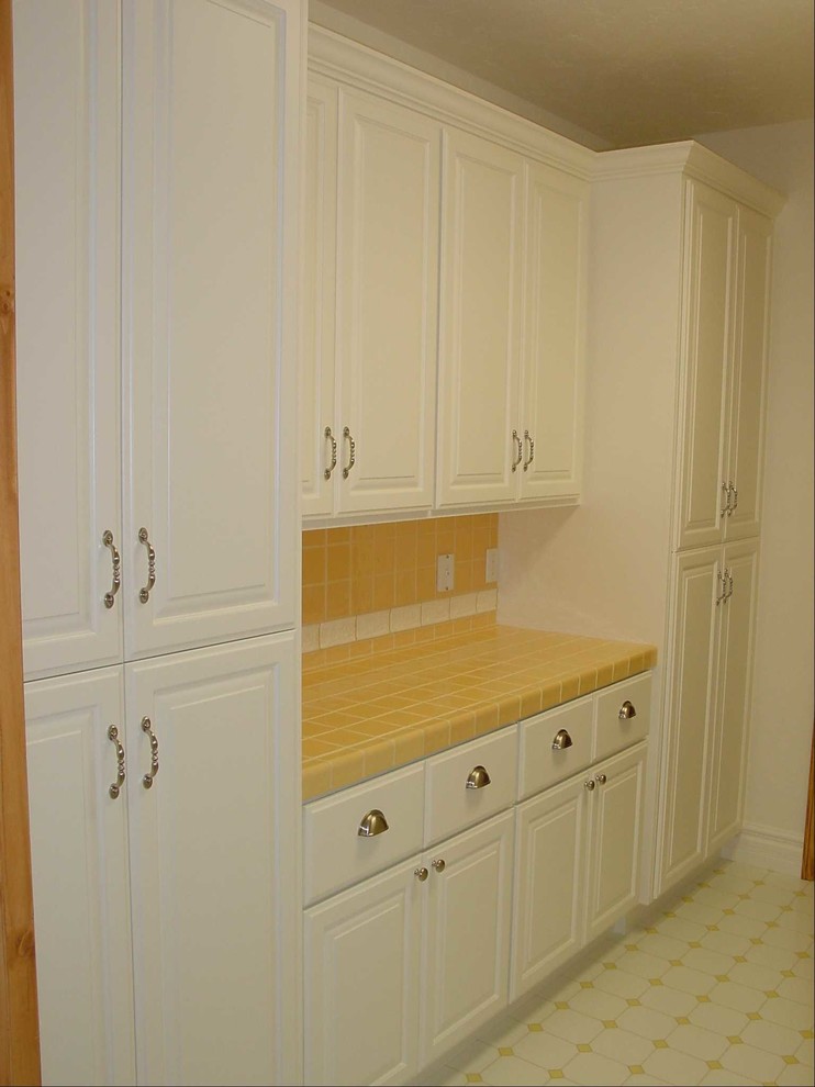 Design ideas for a mid-sized traditional galley utility room in Sacramento with a farmhouse sink, raised-panel cabinets, white cabinets, tile benchtops, porcelain floors and a side-by-side washer and dryer.