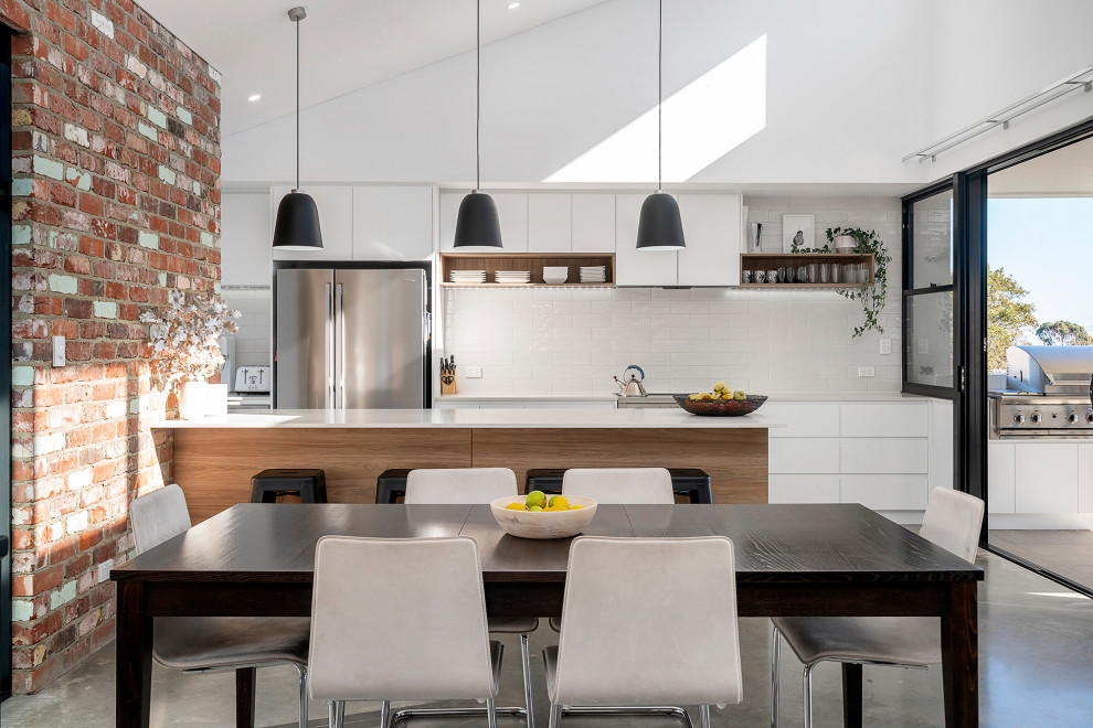 Design ideas for a mid-sized industrial galley open plan kitchen in Perth with concrete floors, flat-panel cabinets, white cabinets, white splashback, subway tile splashback, a peninsula, grey floor and white benchtop.