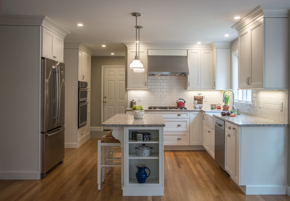 Mid-sized transitional l-shaped medium tone wood floor eat-in kitchen photo in Boston with a farmhouse sink, shaker cabinets, white cabinets, quartz countertops, white backsplash, subway tile backsplash, stainless steel appliances and an island