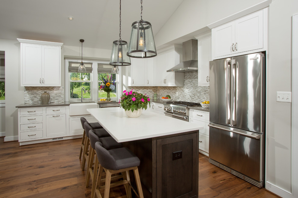 Inspiration for a mid-sized transitional single-wall medium tone wood floor and brown floor open concept kitchen remodel in DC Metro with a farmhouse sink, recessed-panel cabinets, white cabinets, quartz countertops, multicolored backsplash, mosaic tile backsplash, stainless steel appliances and an island
