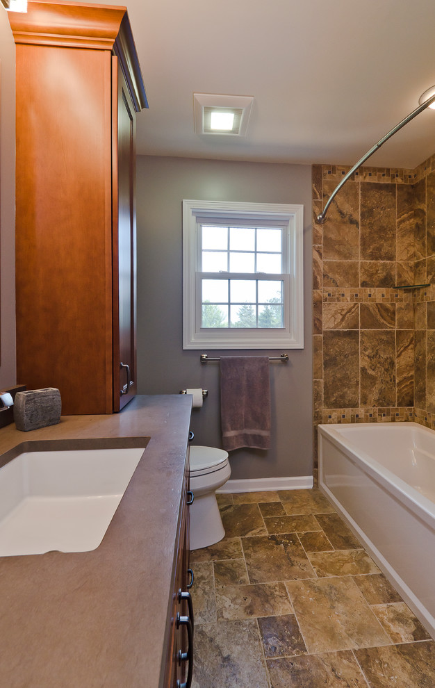 Design ideas for a mid-sized traditional kids bathroom in Chicago with an undermount sink, recessed-panel cabinets, medium wood cabinets, limestone benchtops, an alcove tub, an alcove shower, a two-piece toilet, brown tile, porcelain tile, grey walls and porcelain floors.