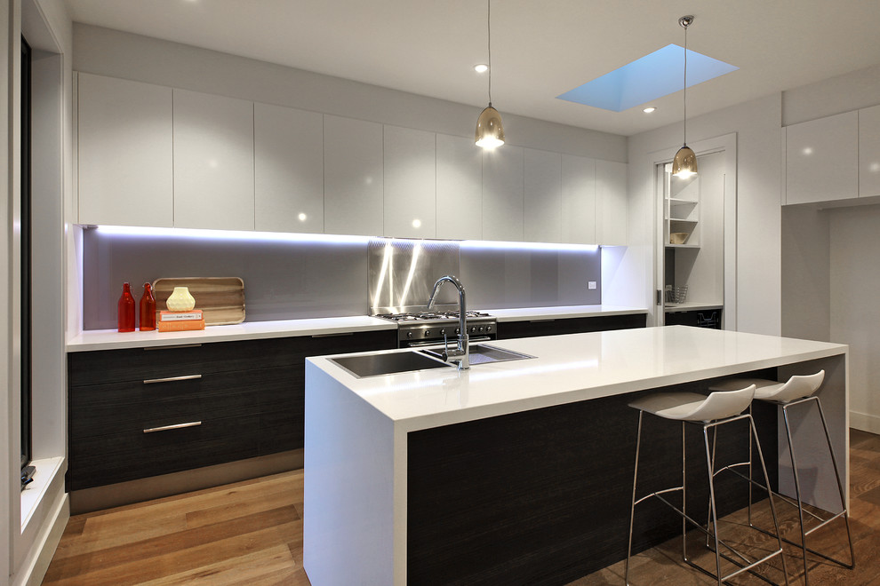 Inspiration for a mid-sized contemporary galley kitchen pantry in Melbourne with a double-bowl sink, flat-panel cabinets, dark wood cabinets, quartz benchtops, grey splashback, glass sheet splashback, stainless steel appliances, medium hardwood floors and with island.
