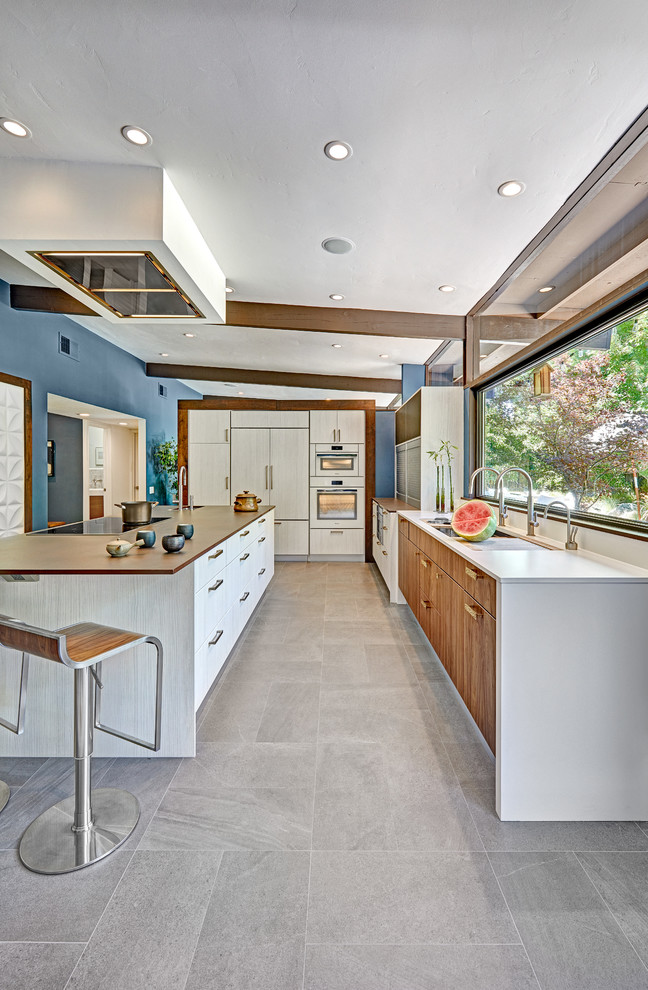 This is an example of a mid-sized midcentury l-shaped open plan kitchen in Sacramento with an undermount sink, flat-panel cabinets, white cabinets, quartz benchtops, white splashback, stone slab splashback, white appliances, porcelain floors, with island and grey floor.