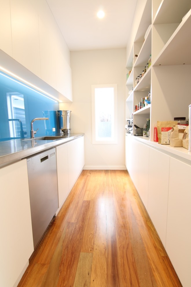 Photo of a modern kitchen in Auckland with a single-bowl sink, blue splashback, glass sheet splashback, stainless steel appliances and light hardwood floors.