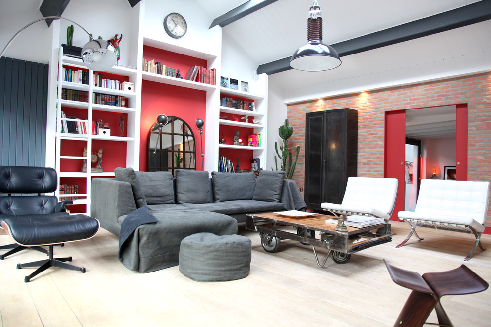 Aménagement d'une grande salle de séjour industrielle ouverte avec une bibliothèque ou un coin lecture, un mur rouge et parquet clair.