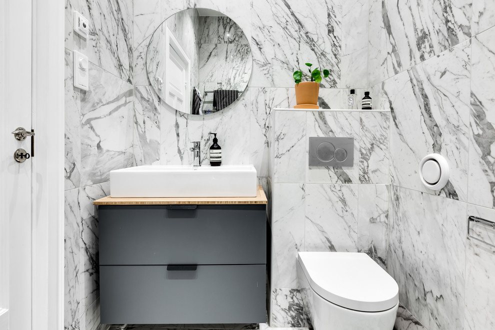 Inspiration for a small scandinavian powder room in Stockholm with flat-panel cabinets, grey cabinets, a wall-mount toilet, gray tile, white tile, multi-coloured tile, a vessel sink, wood benchtops and beige benchtops.