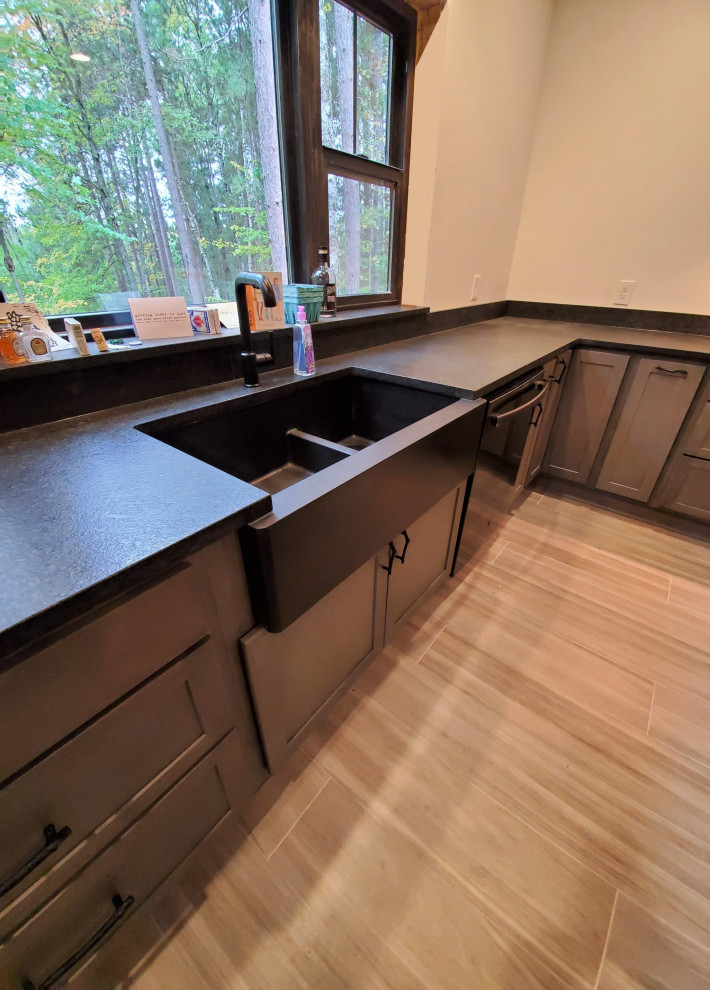 Mid-sized transitional porcelain tile and gray floor kitchen photo with a farmhouse sink, shaker cabinets, gray cabinets, granite countertops, black backsplash, stone slab backsplash, stainless steel appliances, an island and black countertops