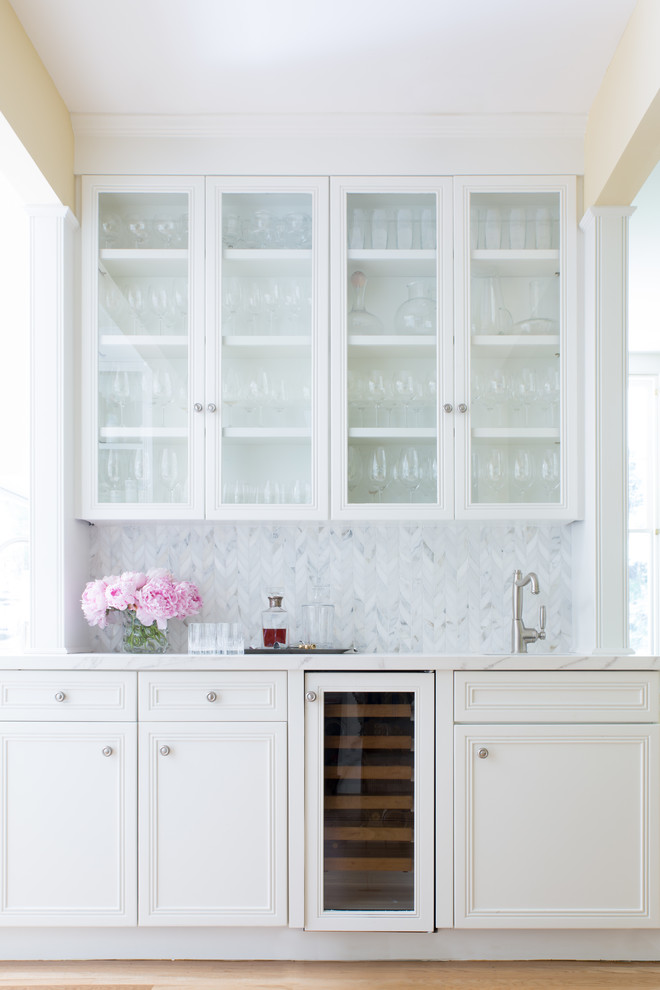 Photo of a classic single-wall wet bar in San Francisco with recessed-panel cabinets, white cabinets, grey splashback and light hardwood flooring.