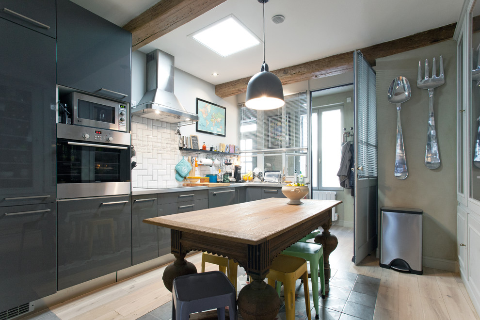 Mid-sized eclectic l-shaped separate kitchen in Montpellier with grey cabinets, white splashback, subway tile splashback, panelled appliances and light hardwood floors.