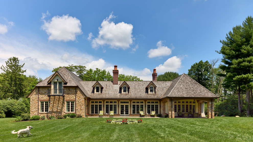 Foto della villa beige classica a due piani con rivestimento in pietra, falda a timpano, copertura a scandole, tetto marrone e con scandole
