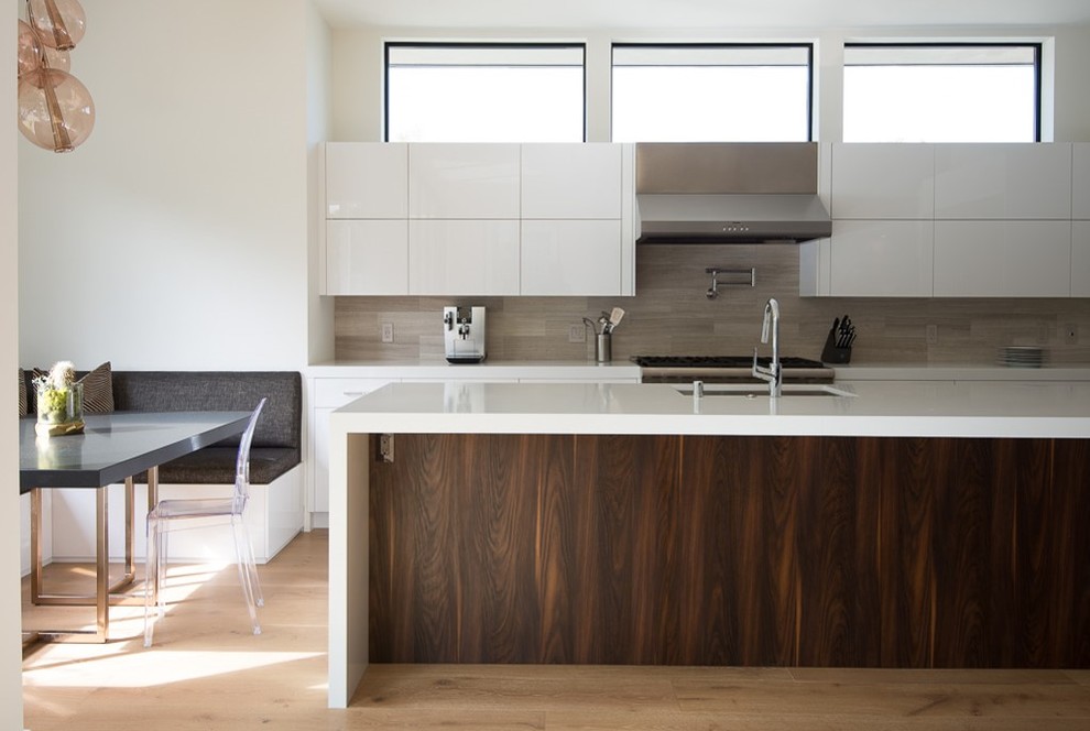This is an example of a contemporary galley kitchen in Los Angeles with an undermount sink, flat-panel cabinets, white cabinets, grey splashback, medium hardwood floors, with island and brown floor.