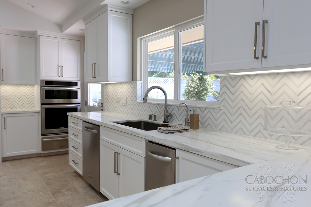Inspiration for a mid-sized transitional l-shaped limestone floor open concept kitchen remodel in San Diego with an island, shaker cabinets, white cabinets, marble countertops, white backsplash, mosaic tile backsplash, stainless steel appliances, an undermount sink and beige walls