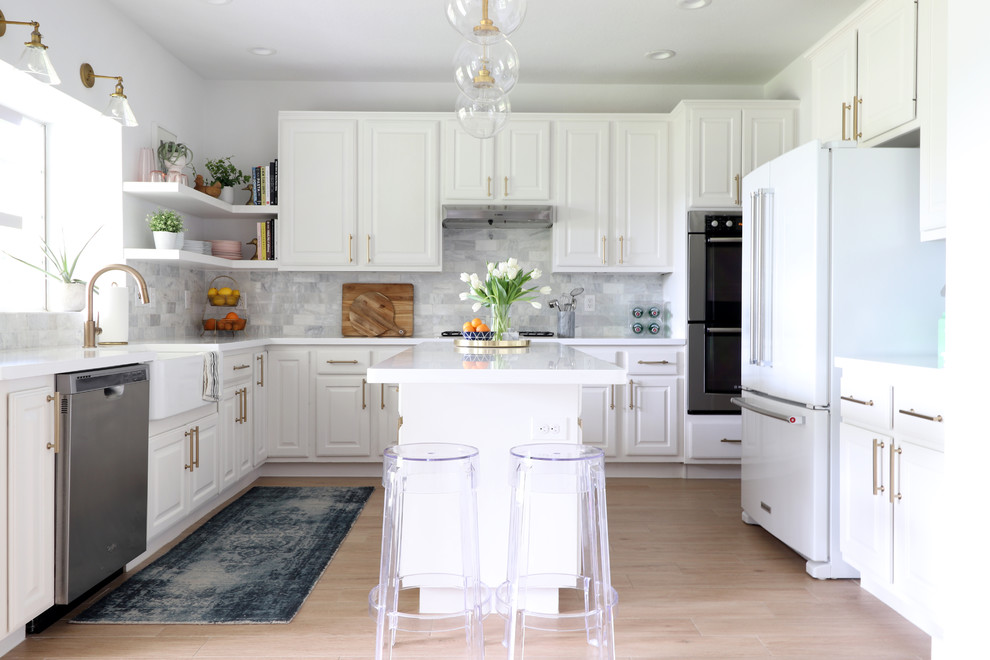 Inspiration for a transitional u-shaped kitchen in Austin with a farmhouse sink, recessed-panel cabinets, white cabinets, grey splashback, subway tile splashback, white appliances, light hardwood floors, with island, beige floor and white benchtop.