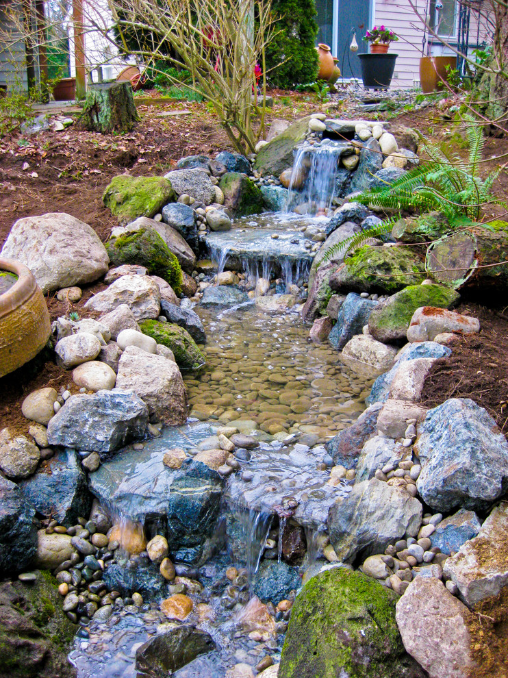 This is an example of a mid-sized rustic full sun backyard stone water fountain landscape in Seattle for spring.