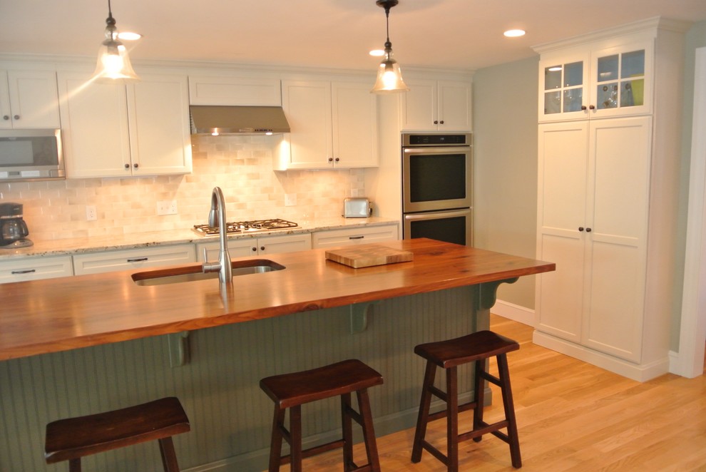 Eat-in kitchen - transitional galley light wood floor eat-in kitchen idea in Boston with an undermount sink, shaker cabinets, white cabinets, wood countertops, white backsplash, ceramic backsplash, stainless steel appliances, an island and brown countertops