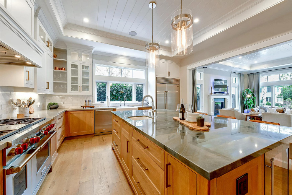 Inspiration for a large arts and crafts l-shaped open plan kitchen in San Francisco with a farmhouse sink, shaker cabinets, medium wood cabinets, white splashback, subway tile splashback, stainless steel appliances, medium hardwood floors, with island, brown floor, grey benchtop and recessed.