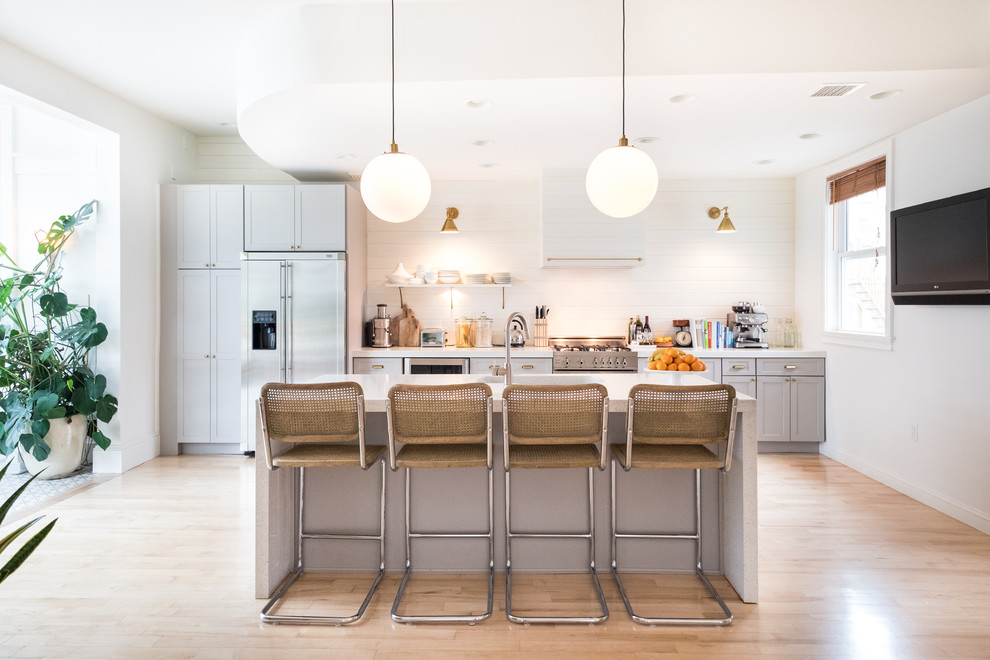 Photo of a transitional galley kitchen in Boston with shaker cabinets, grey cabinets, white splashback, stainless steel appliances, light hardwood floors and with island.