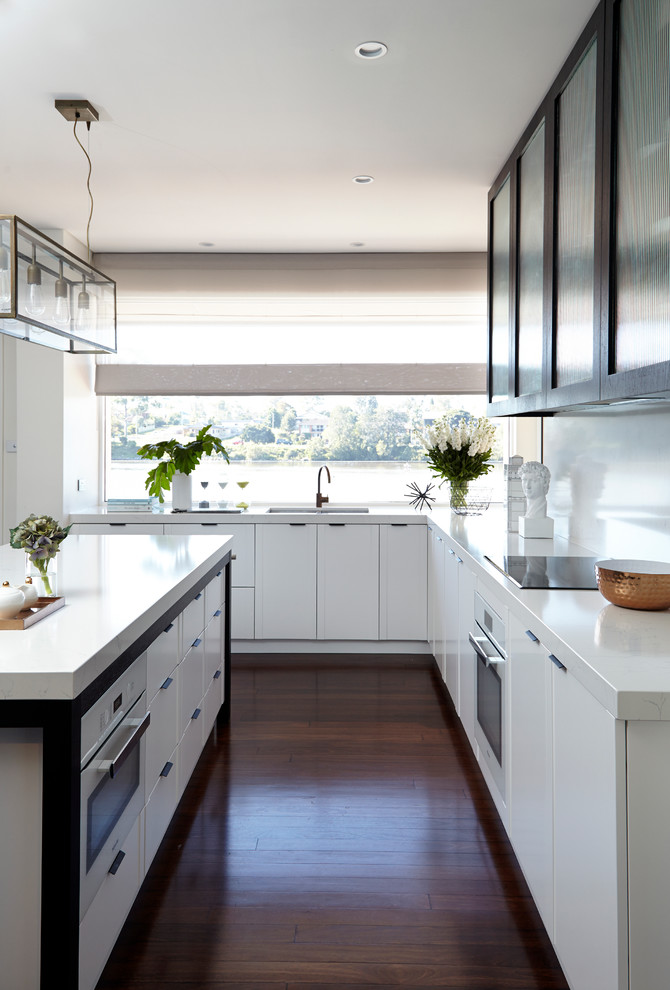 This is an example of a transitional l-shaped kitchen in Sydney with an undermount sink, glass-front cabinets, white cabinets, quartz benchtops, white splashback, stone slab splashback, stainless steel appliances, dark hardwood floors and with island.