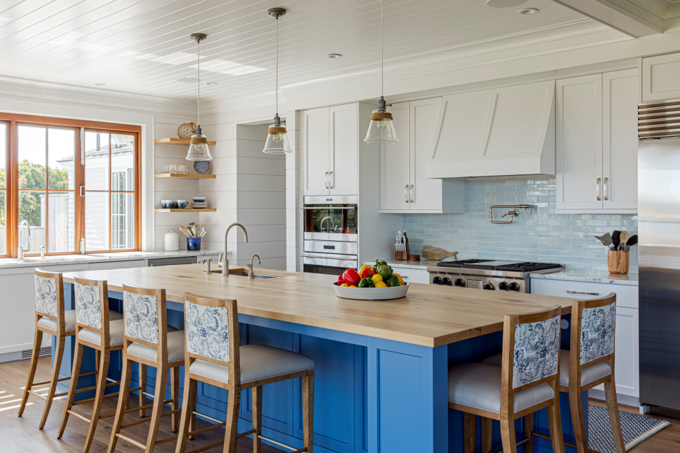 Example of a large beach style l-shaped medium tone wood floor and shiplap ceiling eat-in kitchen design in Boston with a single-bowl sink, recessed-panel cabinets, white cabinets, granite countertops, blue backsplash, glass tile backsplash, stainless steel appliances, an island and white countertops