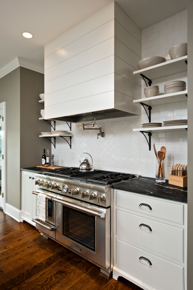 This is an example of an eat-in kitchen in New York with a farmhouse sink, open cabinets, white cabinets, soapstone benchtops, white splashback, glass tile splashback, stainless steel appliances, medium hardwood floors and with island.