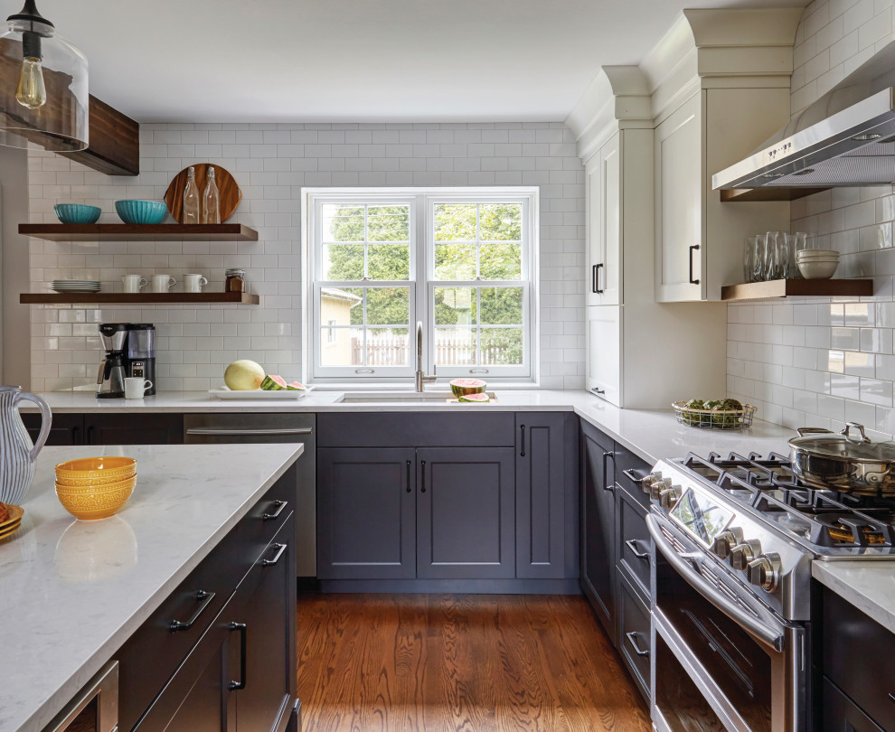 Example of a mid-sized transitional l-shaped medium tone wood floor and brown floor eat-in kitchen design in Chicago with an undermount sink, flat-panel cabinets, gray cabinets, white backsplash, subway tile backsplash, stainless steel appliances, an island and white countertops