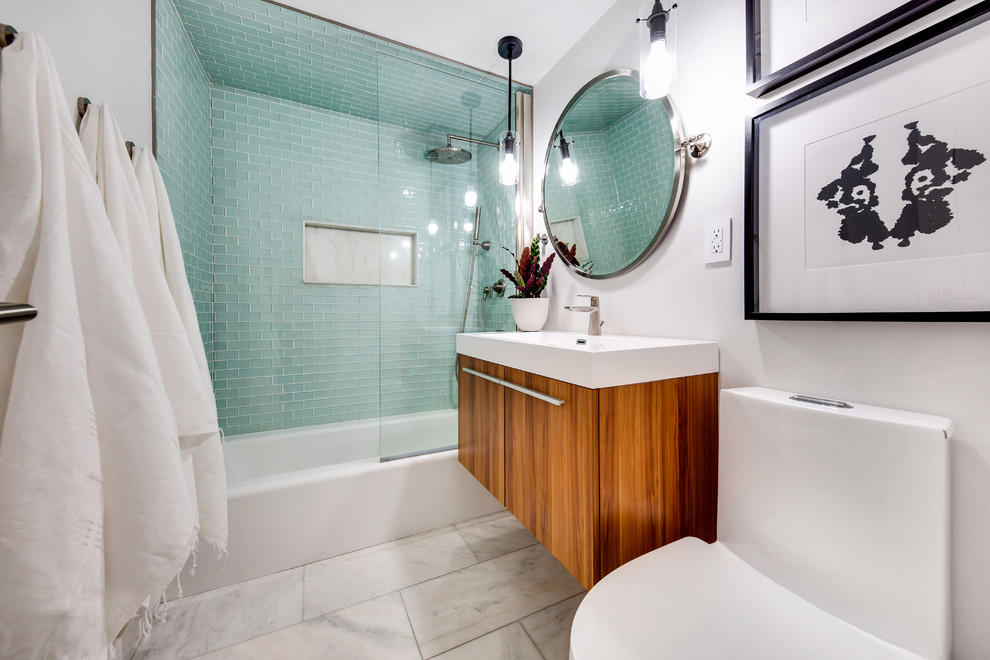 Design ideas for a small modern master bathroom in New York with flat-panel cabinets, medium wood cabinets, an alcove tub, a shower/bathtub combo, a one-piece toilet, green tile, glass tile, grey walls, marble floors, a wall-mount sink, engineered quartz benchtops, white floor, an open shower and white benchtops.